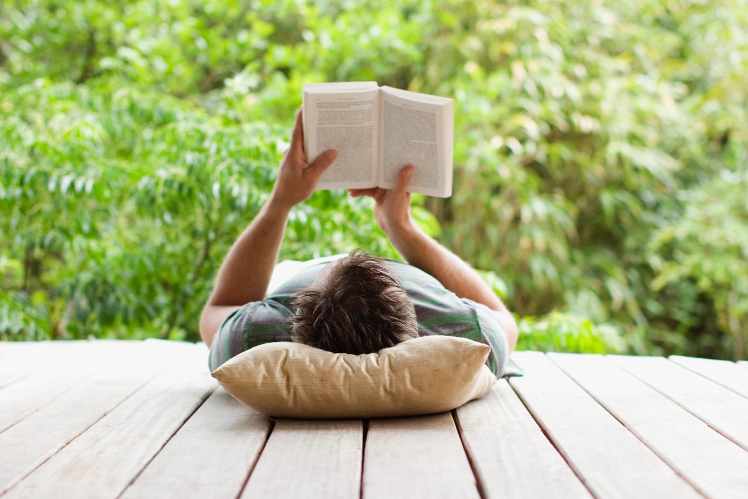 Man reading a book laying on his back - head on pillow